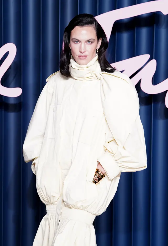 Alexa Chung wears a billowing, cream dress white an over-sized cream cravat set to one side.