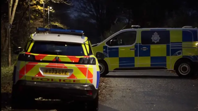 Two police vehicles parked at the end of a cordon