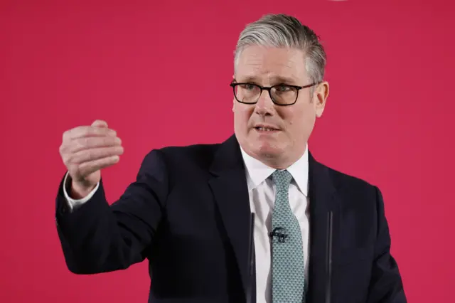 The prime minister standing in front of a red background and holding his left hand in the air