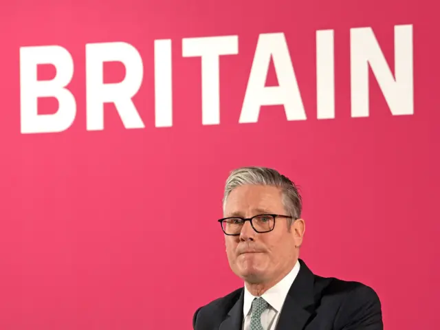 Sir Keir Starmer standing in front of a red background that reads "Britain"