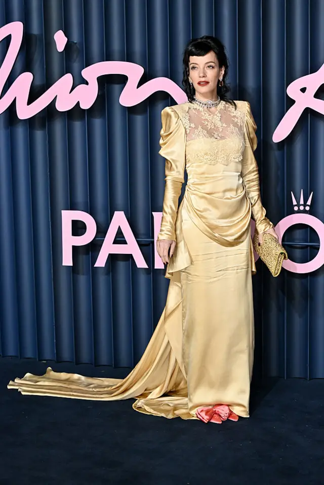 Lily Allen on blue carpet in gold dress