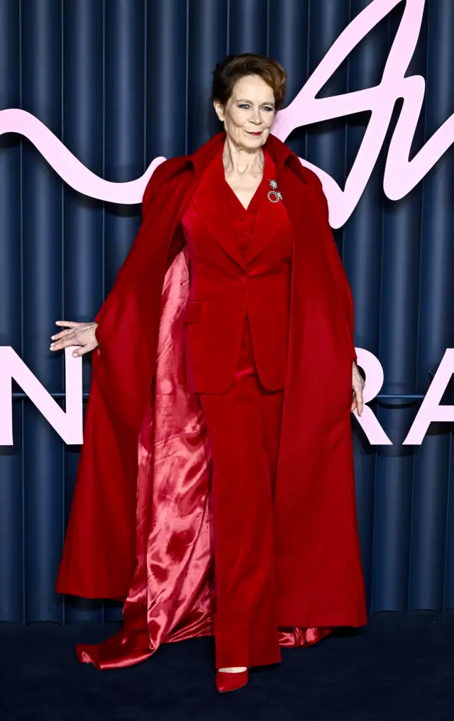Celia Imrie in a bright red suit and a sweeping red cape