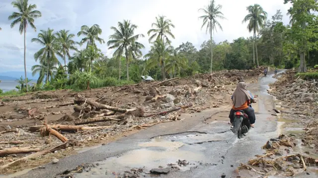 Backview of a couple riding a motorcycle on a muddy road that has been hit by flooding