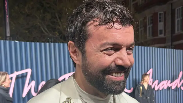 Rocco Iannone wears white suit and gold jewellery