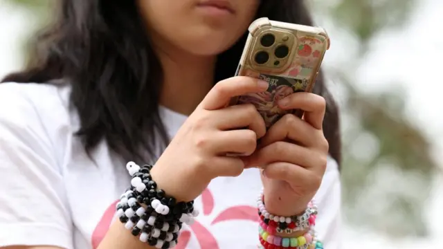 A girl wearing a white t-shirt with bracelets on both wrists holds a mobile phone