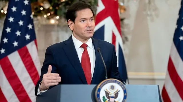 Rubio wears a navy suit and red tie while speaking at a podium