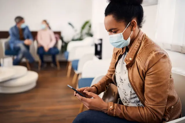 A woman reads her phone and wears a face mask