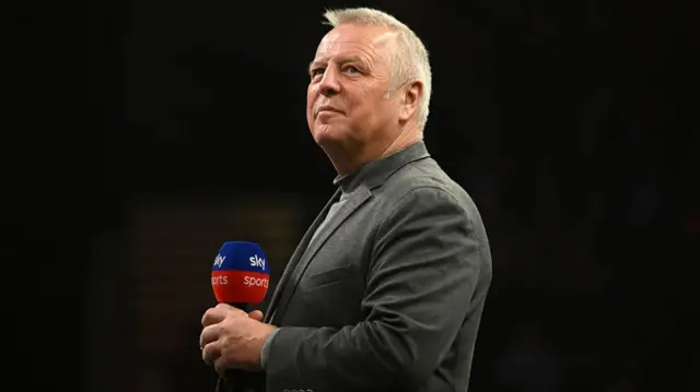 John McDonald stands on stage with a microphone