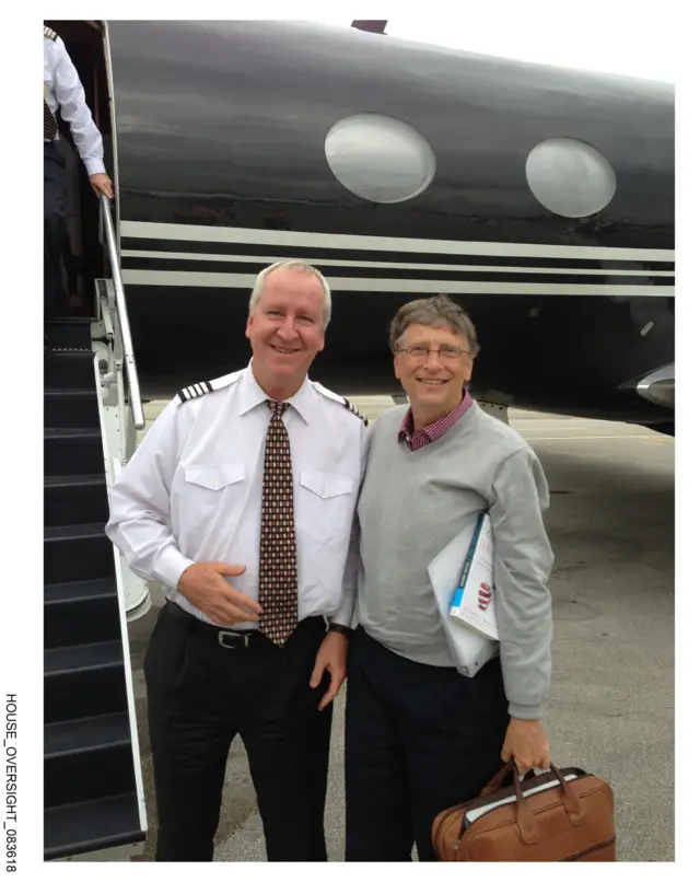 Gates standing in front of a black jet with a man dressed as a pilot.