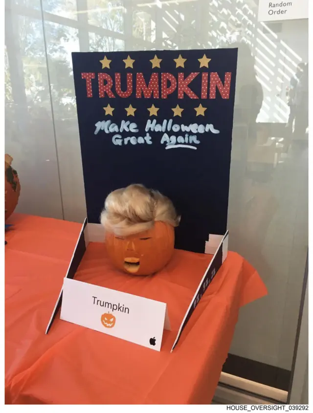 A picture shows a pumpkin with a face carved into it and a and a blonde big. A sign on top reads "TRUMPKIN" in all caps and "Make Halloween Great Again".