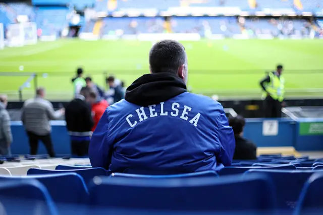 A fan in a Chelsea branded jacket sits in the stands
