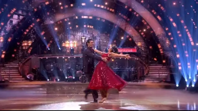 Carlos in a dark blue suit holds up Balvinder, in a glittery red dress, as she leans towards the ground while waltzing