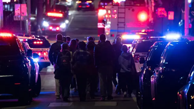 Coterie of police officers and students walking through a street lined with police cars