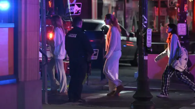 Students in tracksuit pants and jumpers escorted out of a building by police