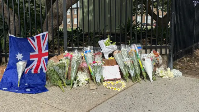An Australian flag lies beside flower tributes on the ground at Bondi Beach