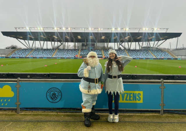 Santa and an elf at Joie Stadium dressed in blue outfits