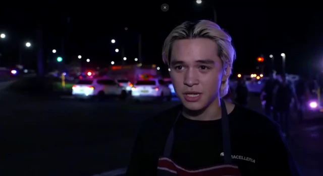 A young man speaking in front of a number of police and emergency service cars