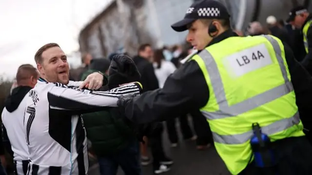 : A Newcastle United fan is ushered along by police as he points to the Champions League badge on his shirt