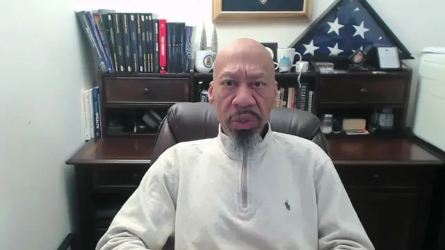 Todd McGhee wears a polo jumper and sits in his office during a Zoom call