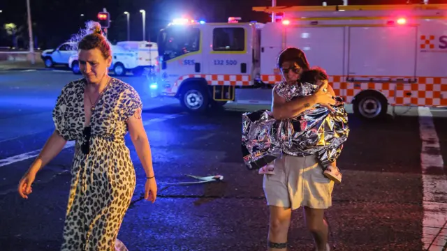 A woman holding a child wrapped in a foil blanket and another woman walking ahead