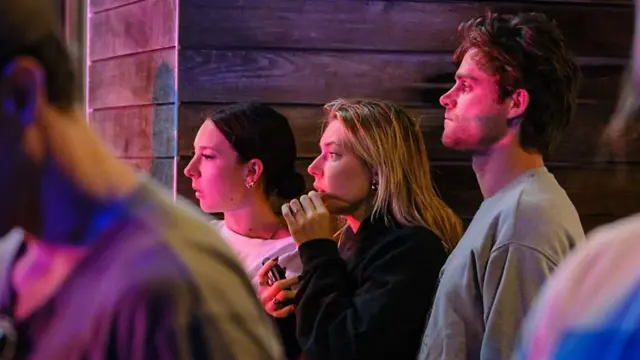 Three people looking concerned/shocked as they watch something out of  the frame