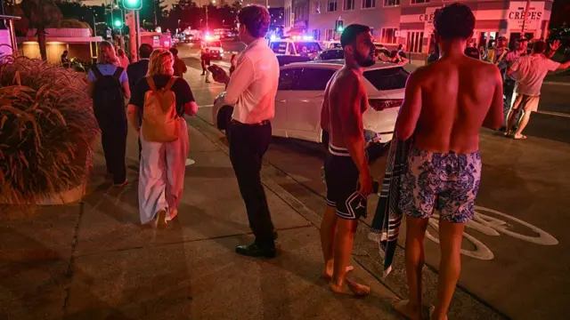 Two men in swimming trunks and without shoes are seen stood on a pavement