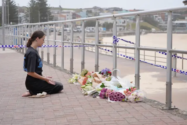 A young woman kneels and prays in front of a cluster of bouquets