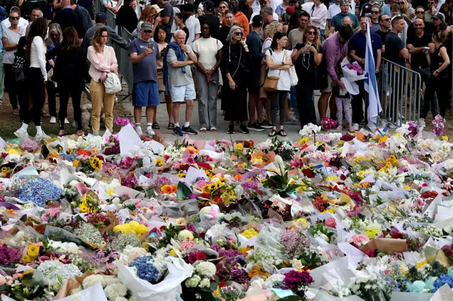 Large group of people standing behind flowers placed on the ground