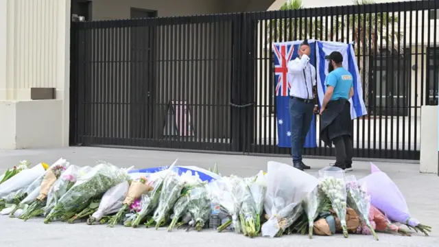 Two man can be seen stood above dozens of floral tributes left near Bondi Beach