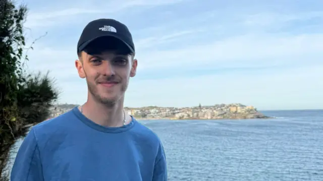 A headshot of Kian who smiles at the camera in front of the sea