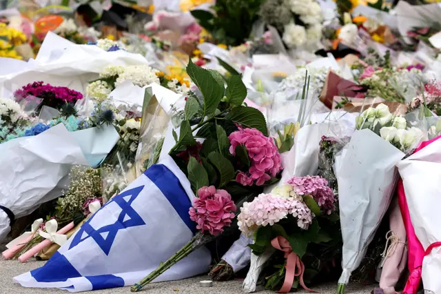 Bouquets of flowers on the ground, one wrapped in an Israeli flag