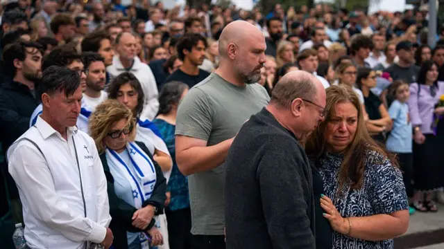 A man and a woman, clearly both upset and grieving, stand together in front of a crowd