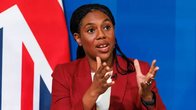 Kemi Badenoch in a red suit and white t-shirt.