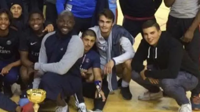 A group of people kneeling down with a football trophy in front of them