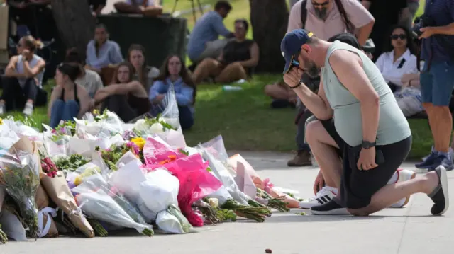 A man kneels after laying flowers at a memorial outside the Bondi Pavilion