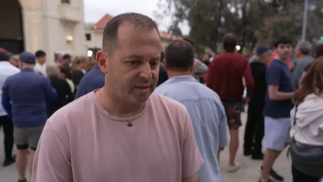 A man in a light pink t-shirt stands in a square outside