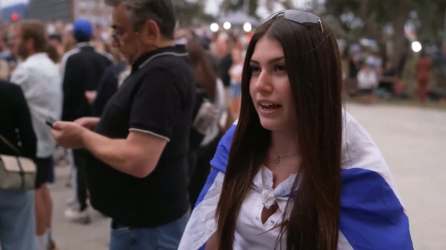 A girl in a white top with a flag draped around her shoulders, she has long brunette hair