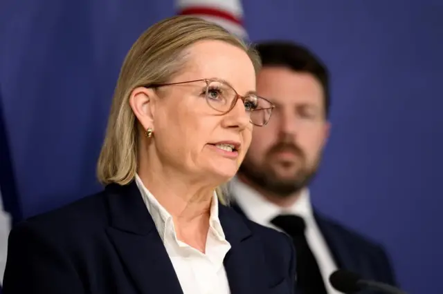 A blonde woman with glasses and a shirt and suit jacket on