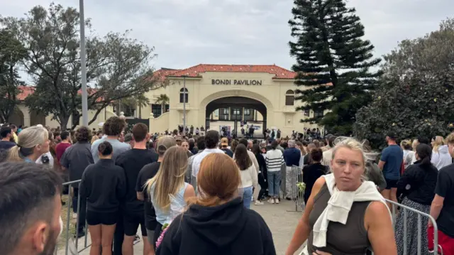 A landscape image of crowds of people standing in front of the Bondi Pavilion