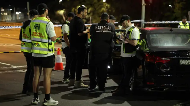 A group of people in black t-shirts and high-vis jackets stand in a car park