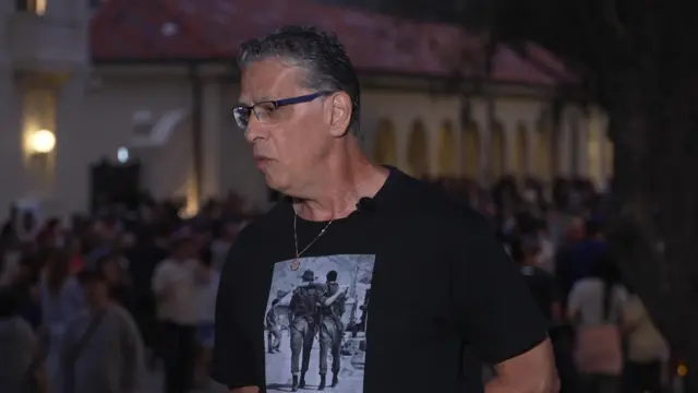 A man stands at the Bondi Beach memorial, talking to BBC reporters