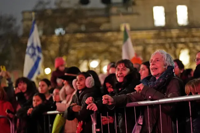 A crowd leans up against railings and looks at red lights