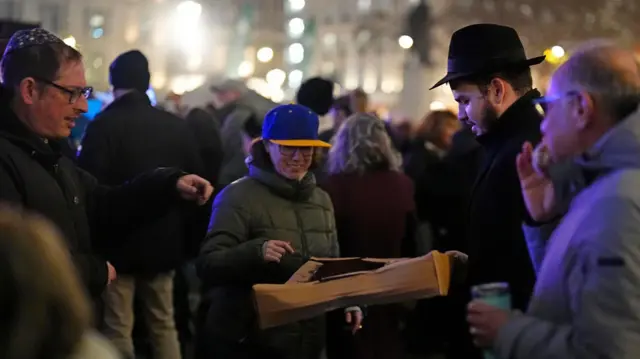 Someone in a cap hands out donuts to a crowd in central London