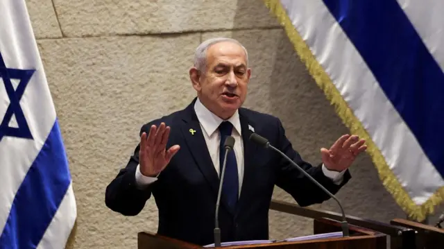 Netanyahu speaking into mic at lectern, in front of an Israel national flag
