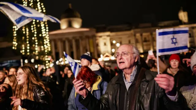 Man holds Israel national flag among crowds of people in Trafalgar Square