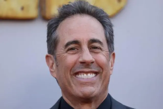A man with greying dark hair smiles looking into the camera