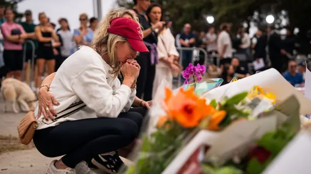 A woman with a red cap clasps her hand as she squats at the memorial site