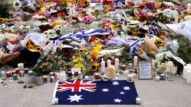The Australian flag lays on the ground, in front of heaps of flowers