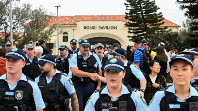 A number of police officers in uniform stand in front of the camera - the Bondi Pavilion can be seen behind