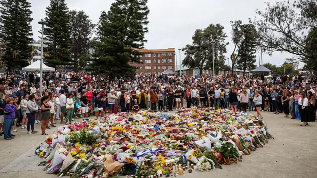 People gather around a huge pile of flower bouquets at a memorial